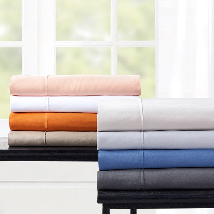 Stack of folded bed sheets in various colors on a table with a window in the background.