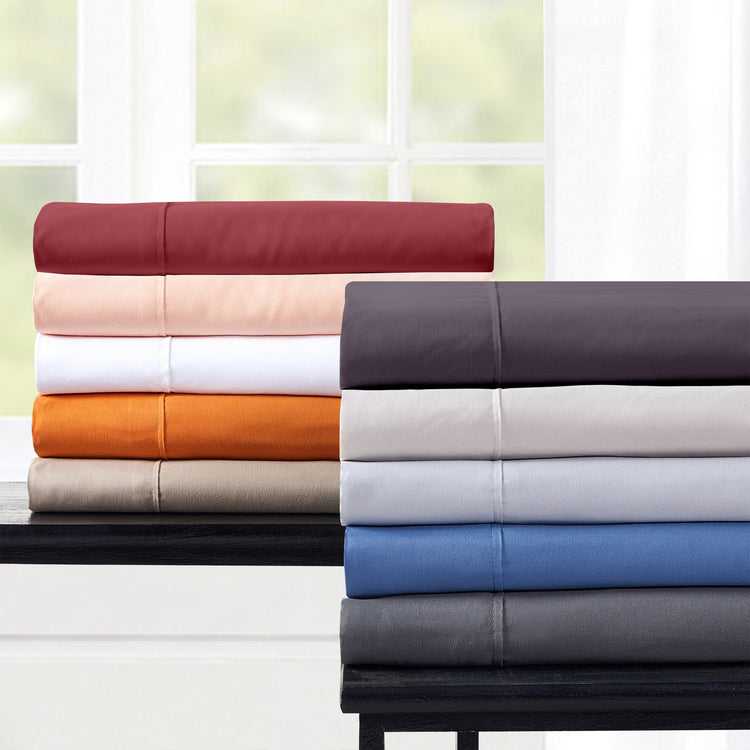 Stacks of folded bed sheets in various colors on a table with a window in the background.