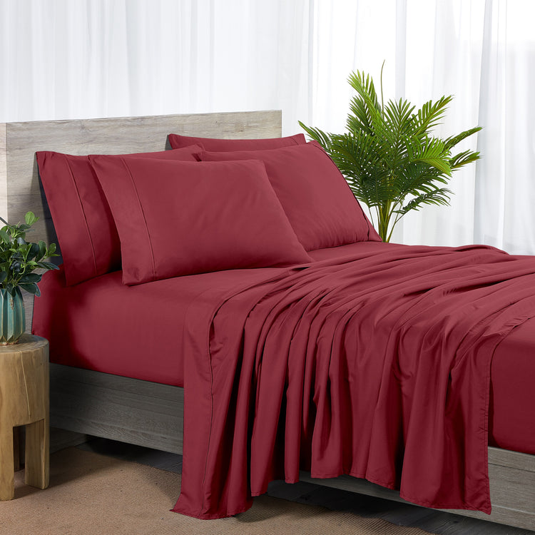 Red bedspread and pillows on a bed with a plant and side table in the background.