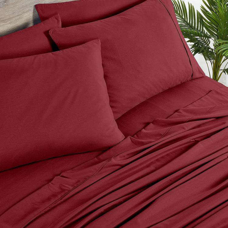 Red bed sheets and pillows on a bed with a plant in the background