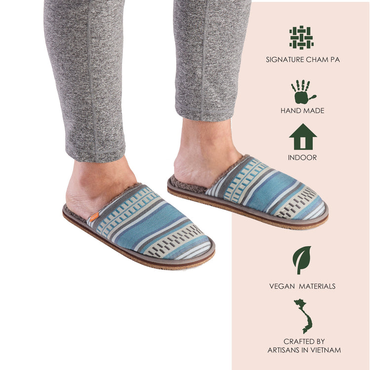Blue patterned slippers worn with gray pants, displayed on a white background with brand information.