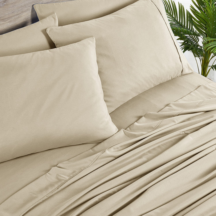 Beige bedding set with pillows on a bed, featuring a tropical plant in the background.