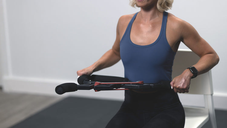 Woman in blue tank top and black leggings using a resistance band in a gym setting.