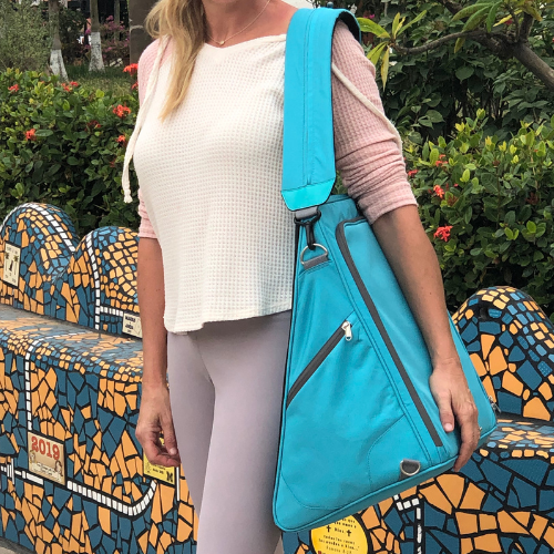 Person holding a blue bag outdoors with a colorful bench and greenery in the background