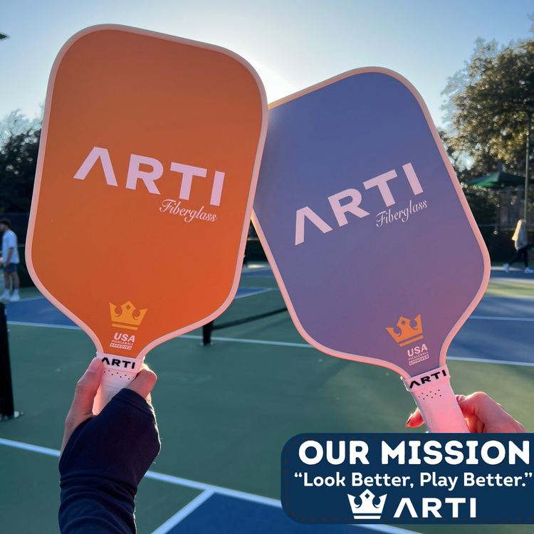 Two pickleball paddles held up with 'ARTI' branding on a tennis court.