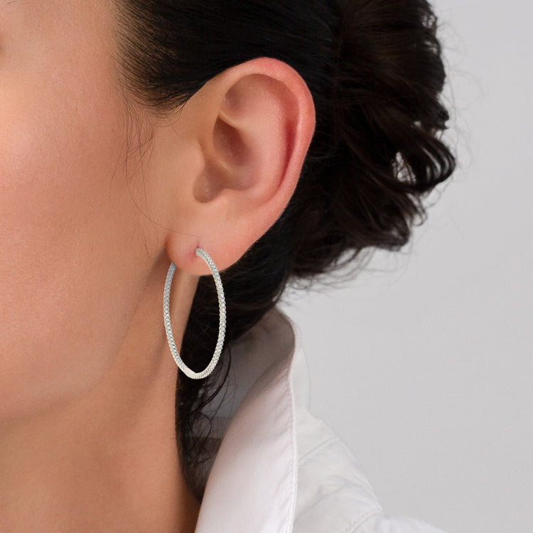 Silver hoop earring worn by a person with a neutral background
