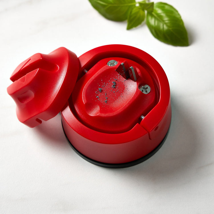 Red kitchen tool with a lid on a white surface with basil leaves.