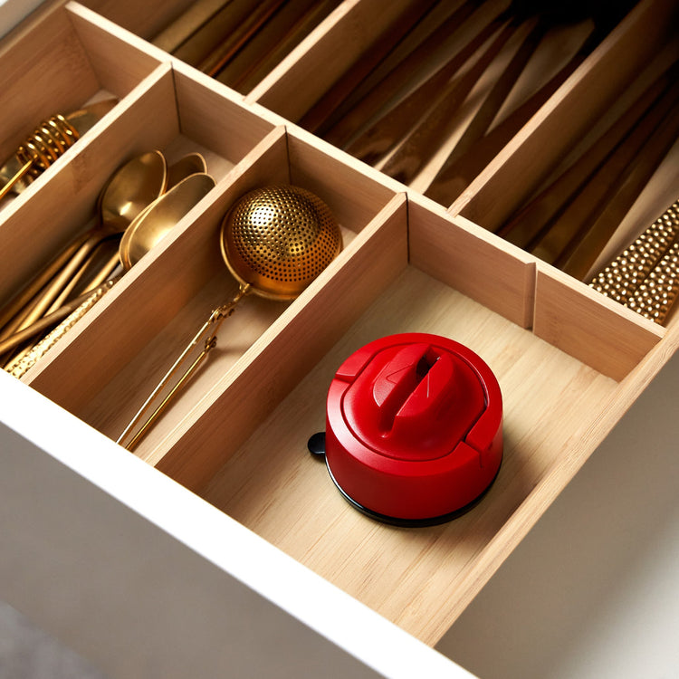 Red lid on a wooden cutlery drawer with gold spoons and tea infuser.