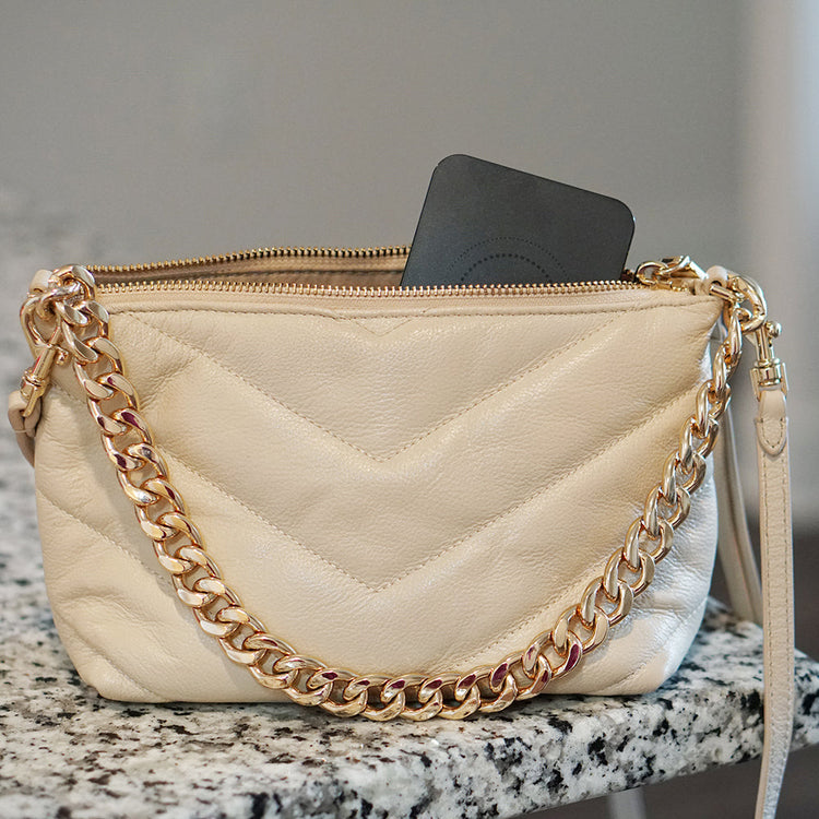 Beige handbag with gold chain strap on a marble surface