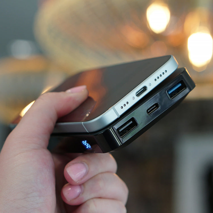 Hand holding a power bank with multiple ports against a blurred indoor background