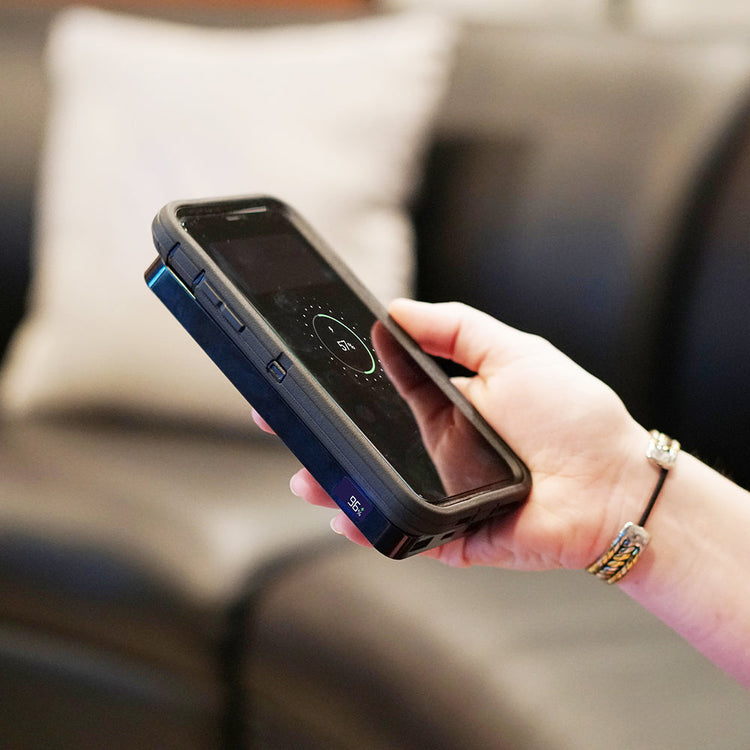 Hand holding a smartphone with a charging case, blurred background