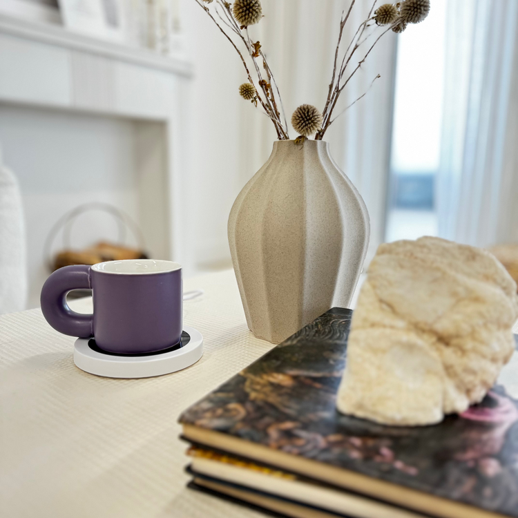 Purple mug on a white coaster with a beige vase and decorative elements on a table.
