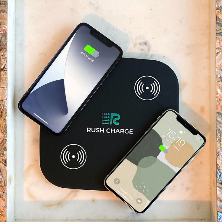 Two smartphones on a Rush Charge wireless charging pad with a blurred natural background.
