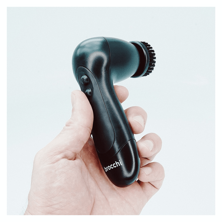 Hand holding a black massage gun with 'Brocchi' branding on a light gray background