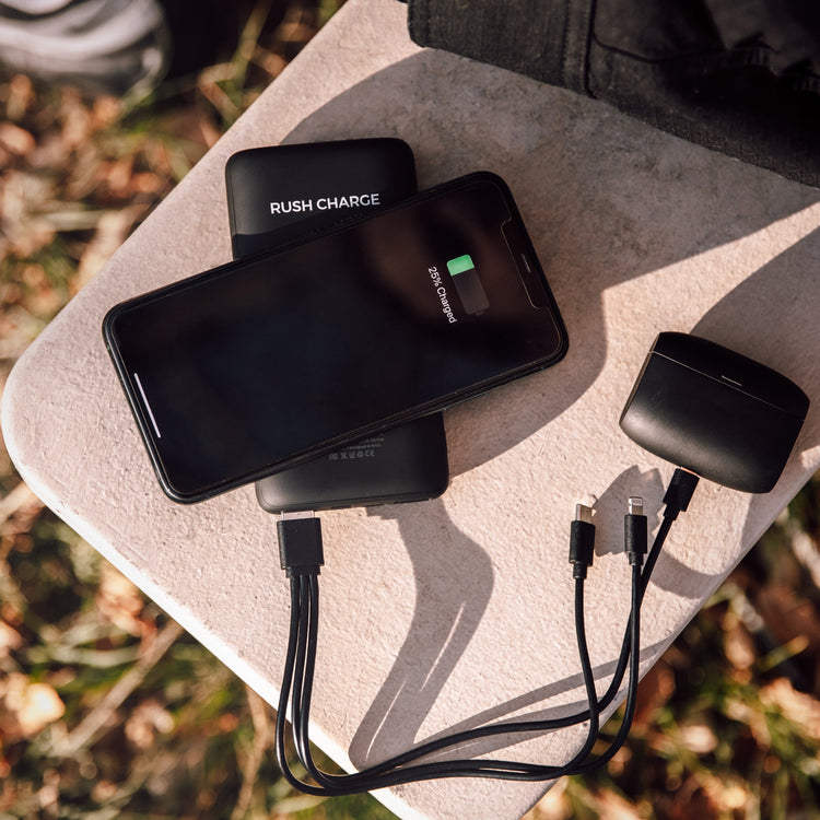 A portable power bank with a attached UV light sanitizing device, and cables connected to a smartphone and earbuds, placed on an outdoor surface.