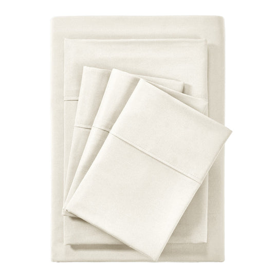 A cream-colored bamboo sheet set on a bed, including a fitted sheet, flat sheet, and pillowcases, with a wooden headboard and houseplants in the room.