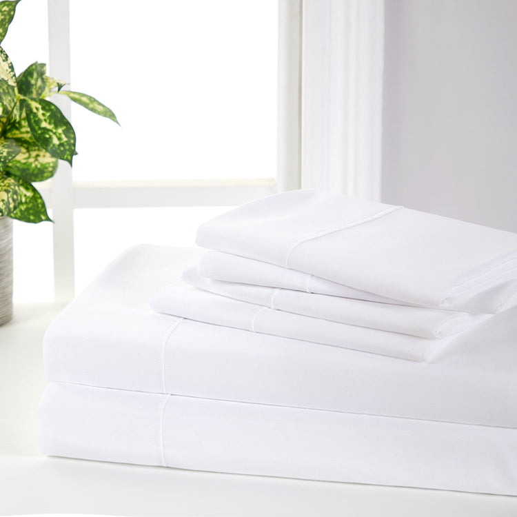 Stack of white bed sheets on a white surface with a plant in the background
