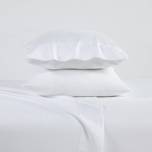A white 6-piece bamboo sheet set on a bed, including a fitted sheet, flat sheet, and pillowcases, presented in a bright room setting with decorative plants and a nightstand.