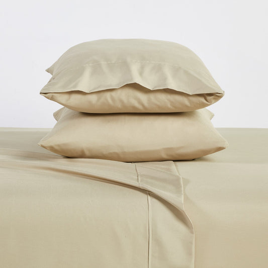 A warm taupe colored 6-piece bamboo sheet set on a bed, with a flat sheet, fitted sheet, and pillowcases displayed. The bed is set against a room backdrop with a plant and nightstand on the side.