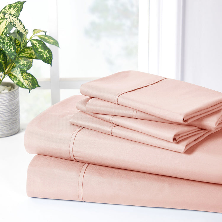 Stack of pink bed sheets on a white surface with a plant in the background