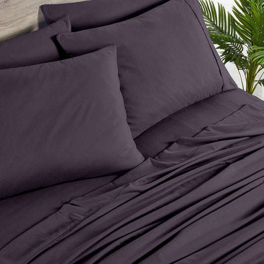 Purple bedding set on a bed with a wooden headboard and plant decor.