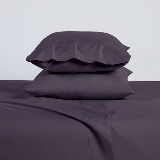Purple bedding set on a bed with a wooden headboard and plant decor.
