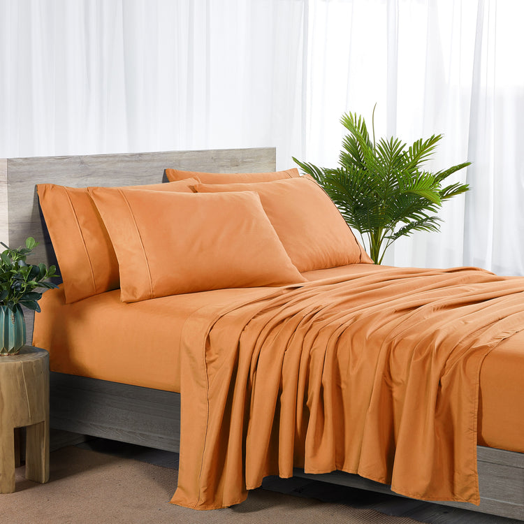 Orange bedding set on a bed with a plant and side table in the background