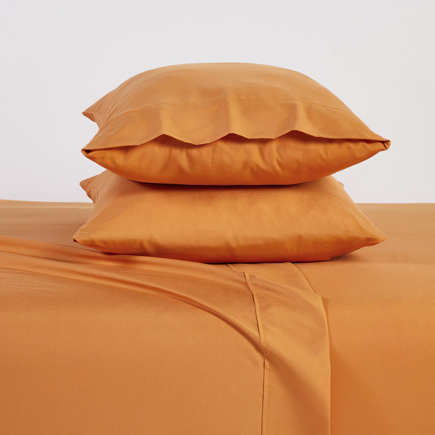 Two orange pillows stacked on a matching orange bedspread against a light gray background