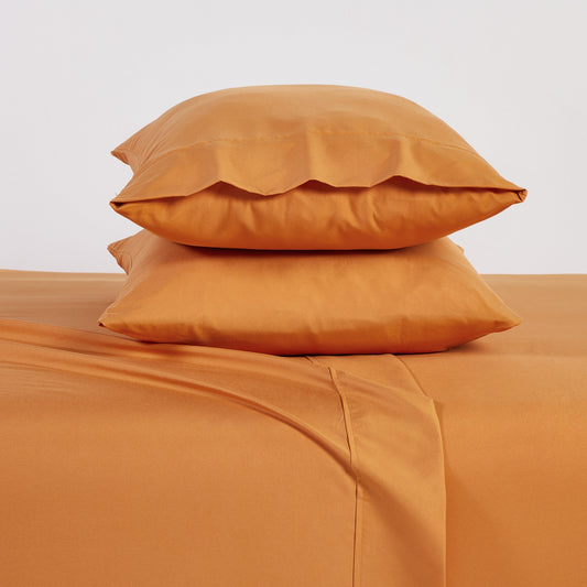 Orange bedding set on a bed with matching pillows in a bedroom setting.