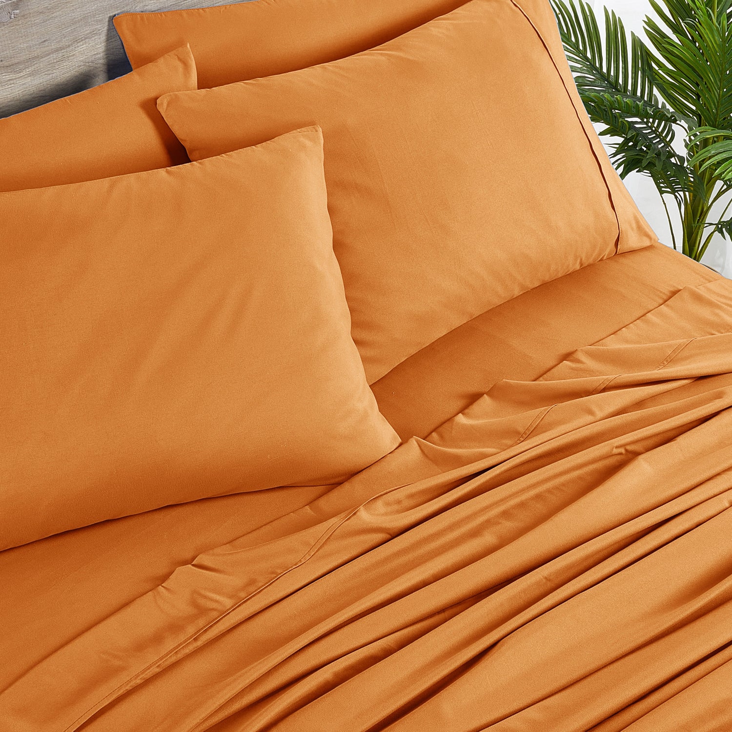 Orange bedding set with pillows on a bed, outdoor setting with plants.