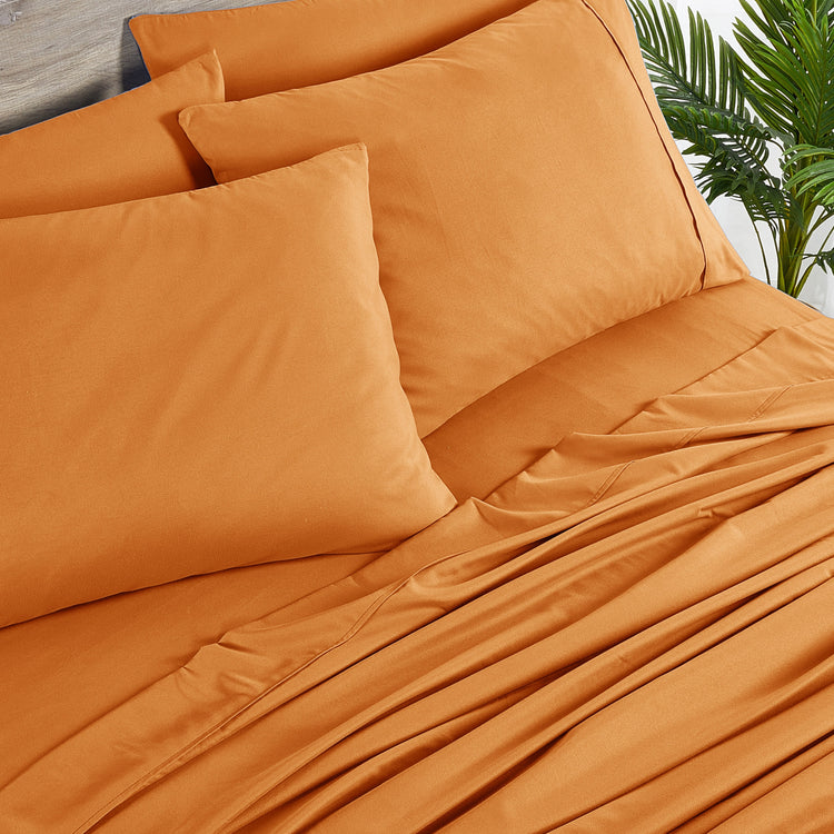 Orange bedding set with pillows on a bed, outdoor setting with plants.