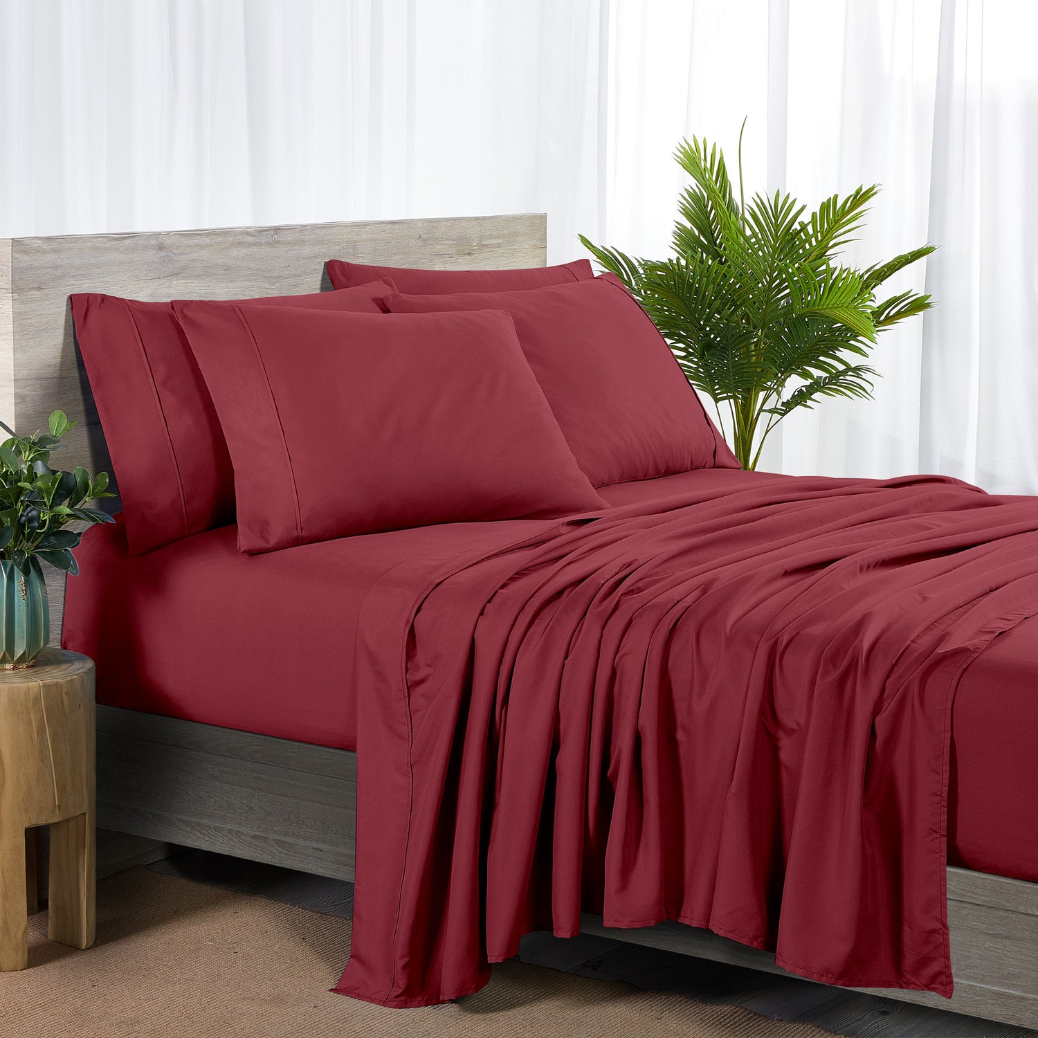 Red bedspread and pillows on a bed with a plant and side table in the background.
