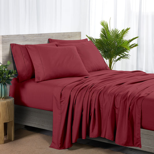 Red bedspread and pillows on a bed with a plant and side table in the background.