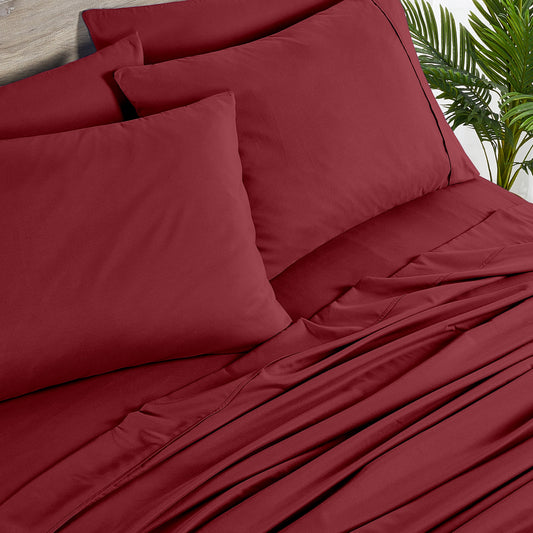 Red bedspread and pillows on a bed with a plant and side table in the background.
