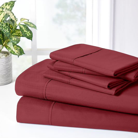 Red bedspread and pillows on a bed with a plant and side table in the background.