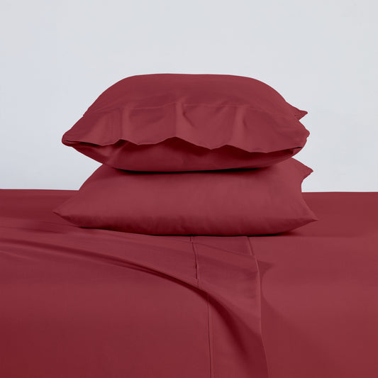 Red bedspread and pillows on a bed with a plant and side table in the background.