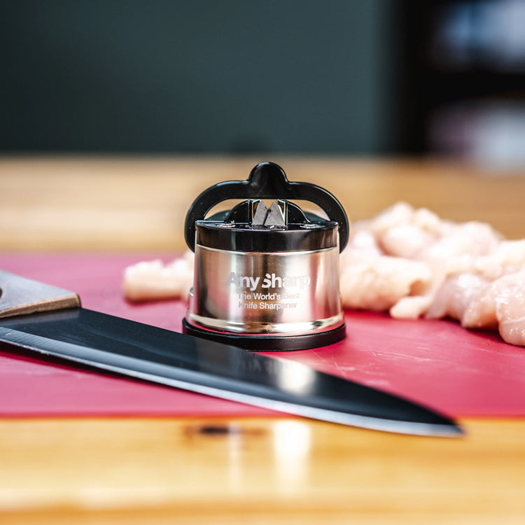 Small sharpener on a cutting board with a knife and chicken pieces in the background