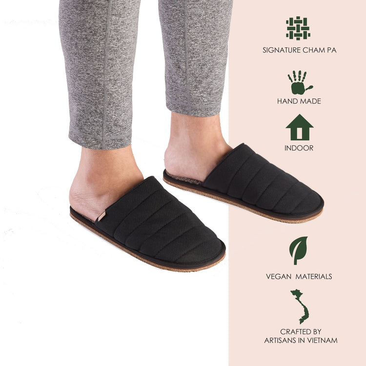 Black slippers worn with gray pants on a white background, featuring brand and material information.