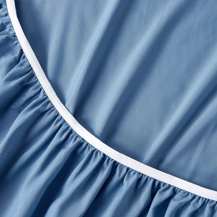 Close-up of a blue fitted sheet with white trim on a bed.