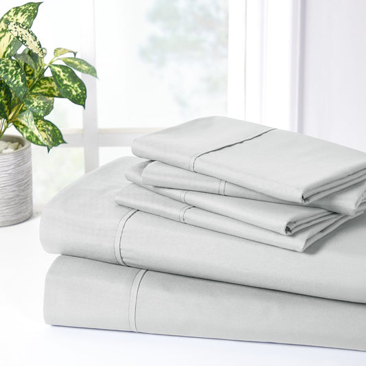 A silver 6-piece bamboo sheet set on a bed, including a fitted sheet, a flat sheet, and pillowcases, presented in a well-lit room with a plant and nightstand beside the bed.
