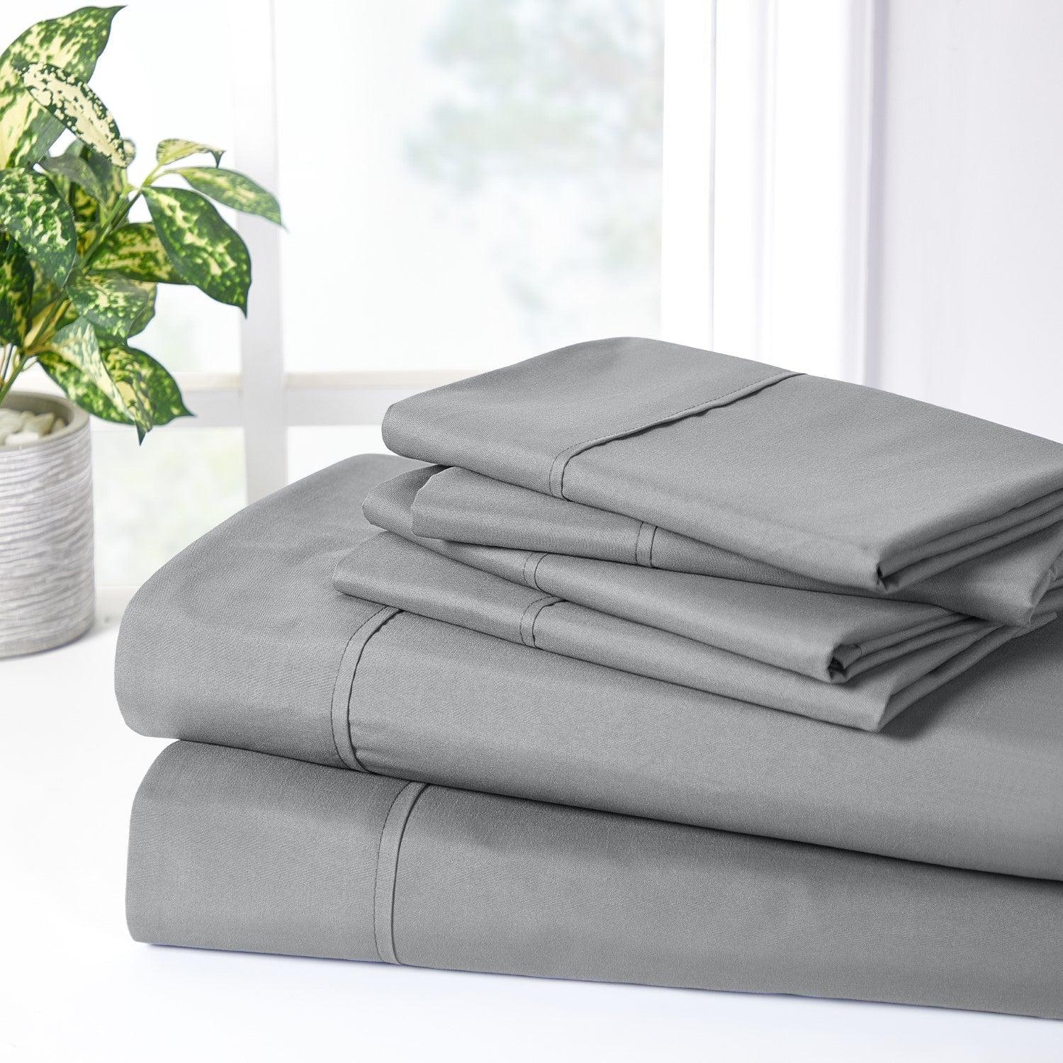 Stack of gray bed sheets on a white surface with a plant in the background