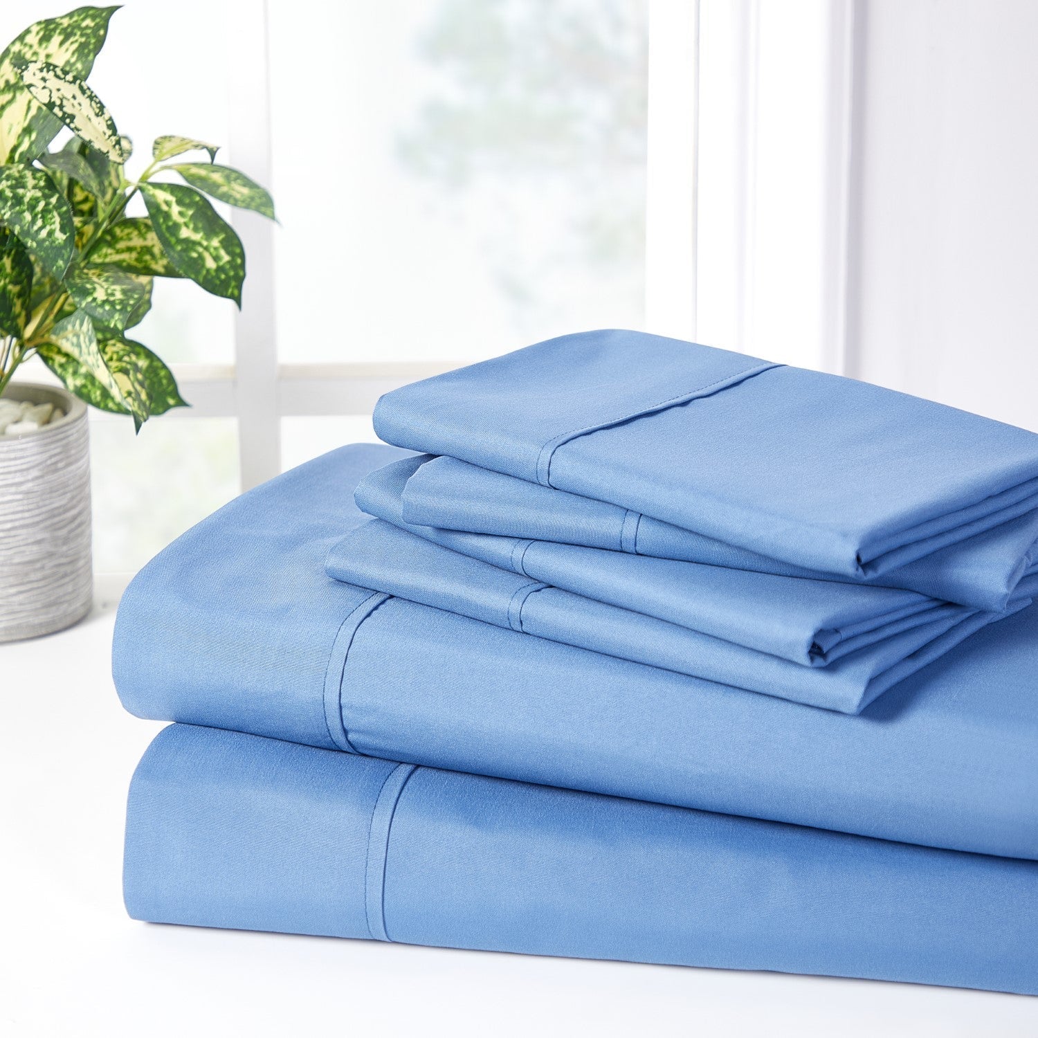 Set of light blue bed sheets on a white surface with a plant in the background