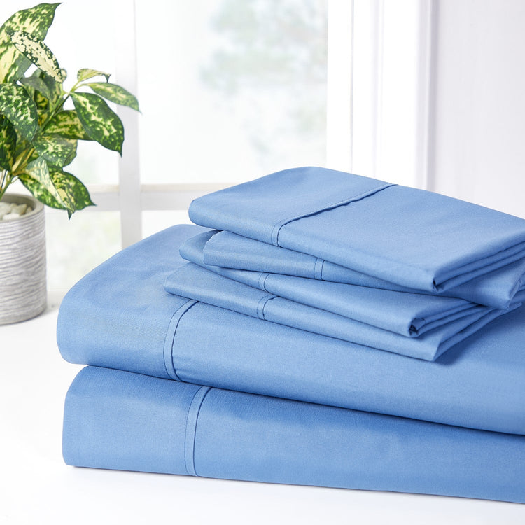 Set of light blue bed sheets on a white surface with a plant in the background