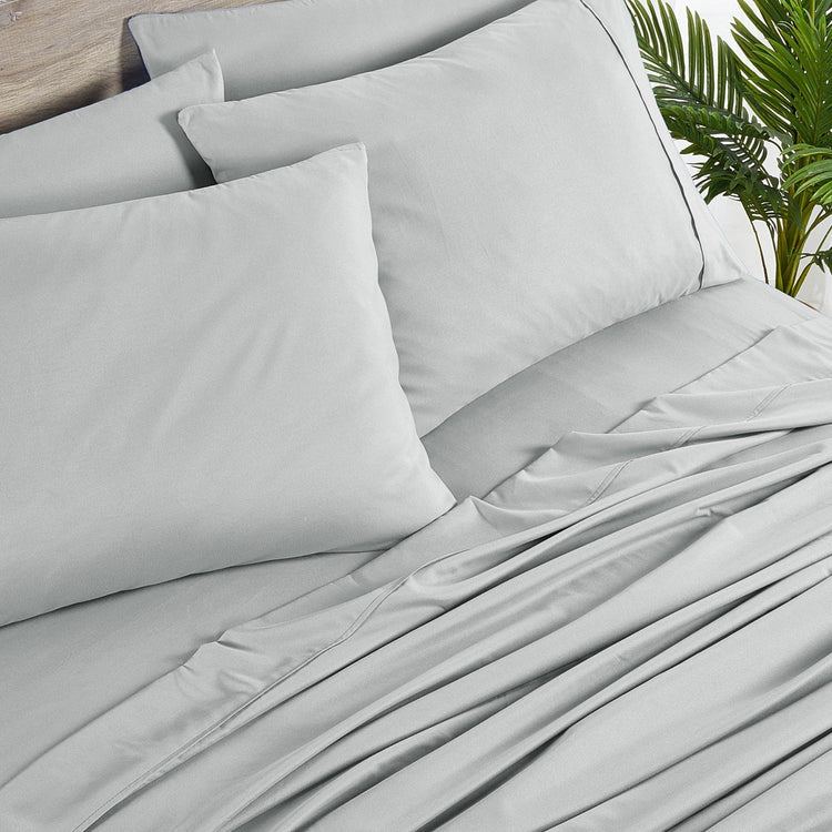 Gray bedding set with pillows on a bed, featuring a plant in the background.