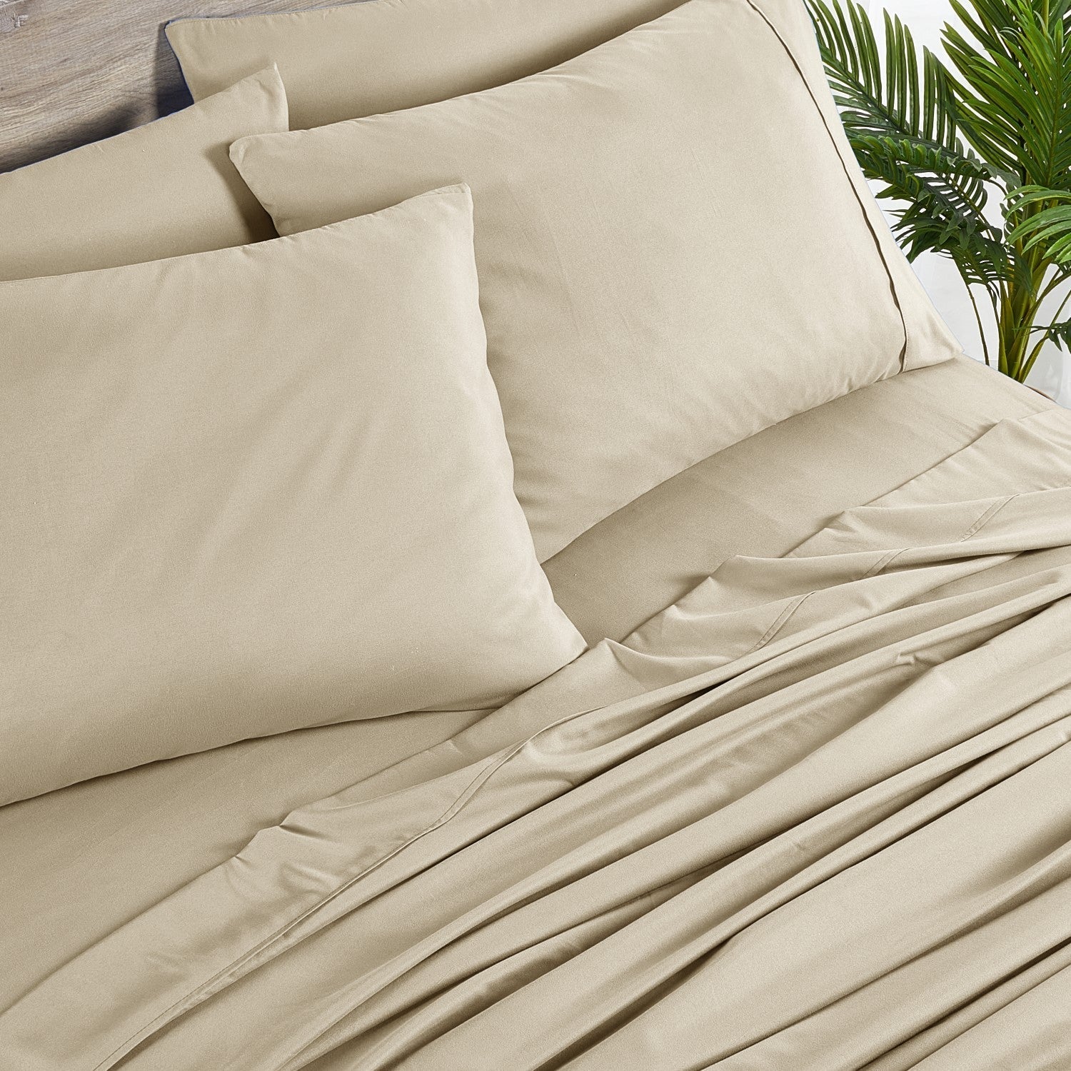 Beige bedding set with pillows on a bed, featuring a tropical plant in the background.
