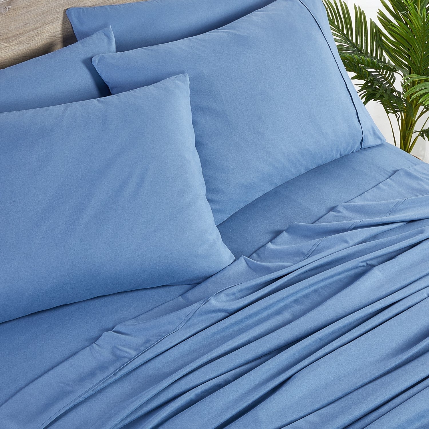 Blue bed sheets and pillows on a bed with a plant in the background