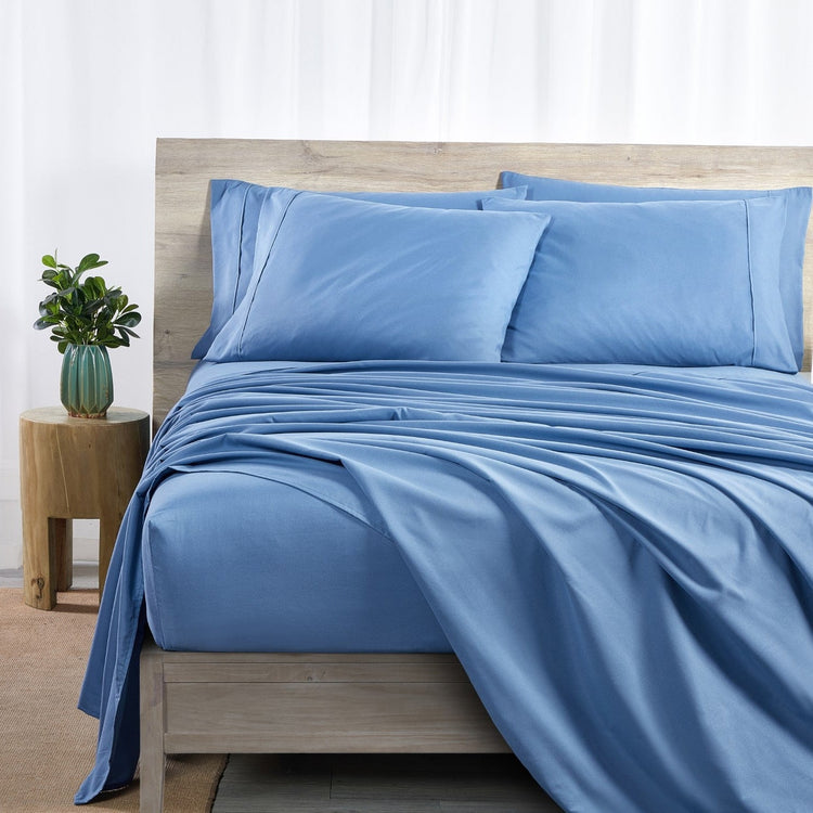 Blue bedding set on a bed with a wooden headboard and side table in a room.
