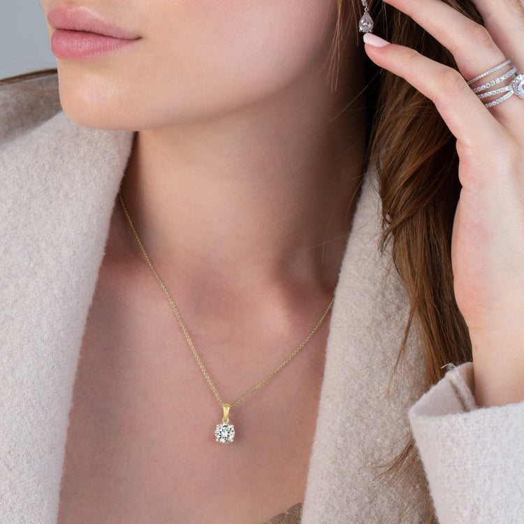 Close-up of a woman wearing a gold necklace with a diamond pendant and earrings.