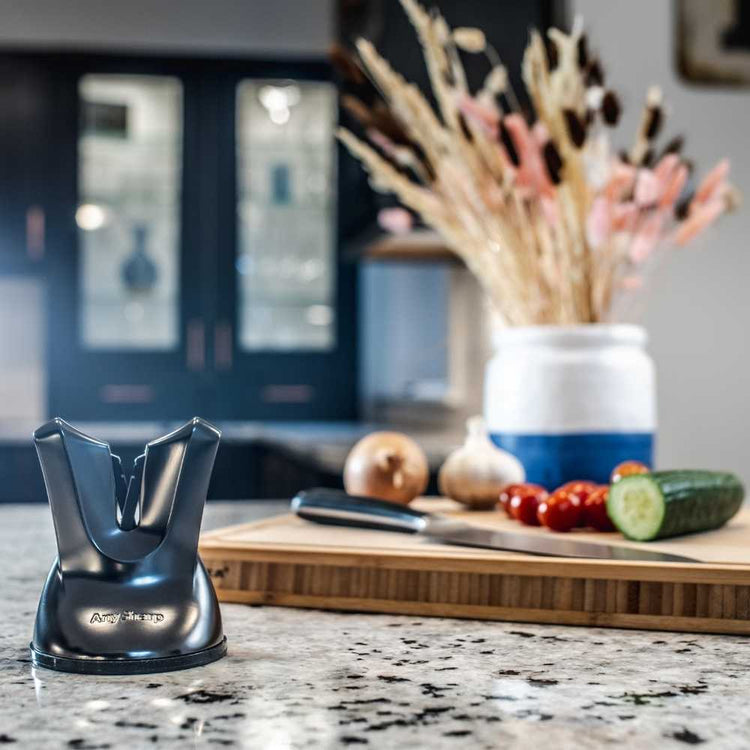 Knife sharpener on a kitchen counter with a cutting board and vegetables in the background