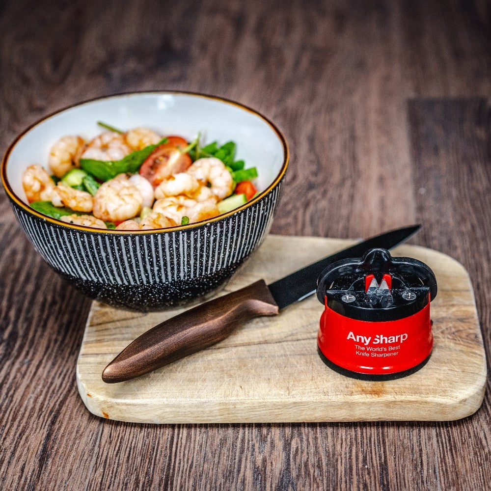 Bowl of salad with a knife and sharpener on a wooden surface